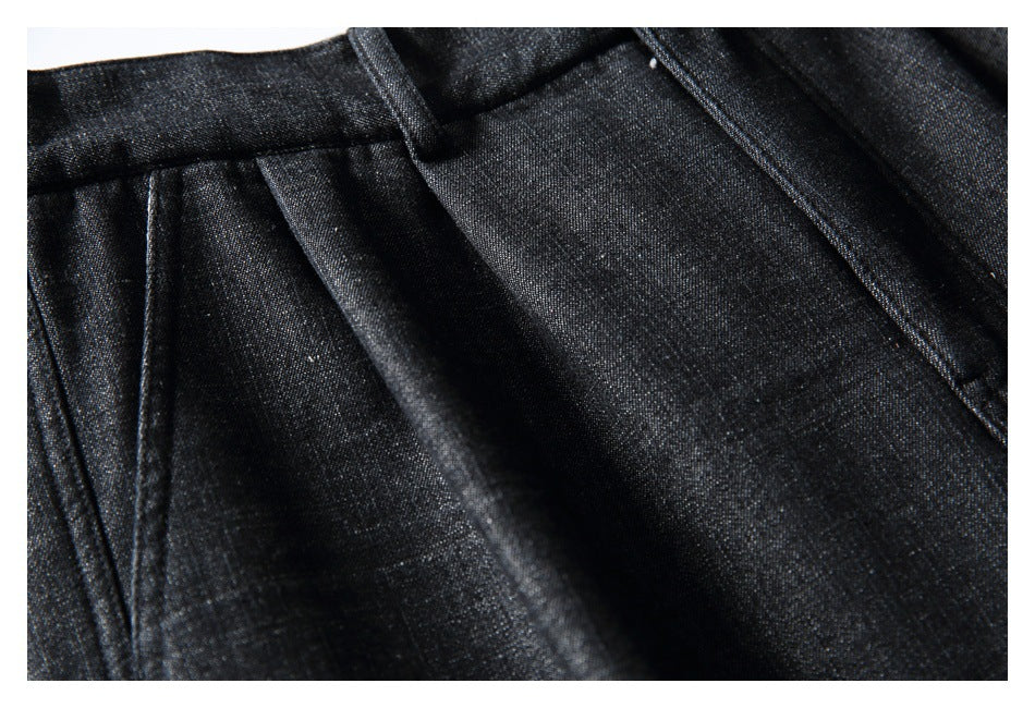 Close-up of black textured trousers showing a belt loop, waistband, and stitched pleats.