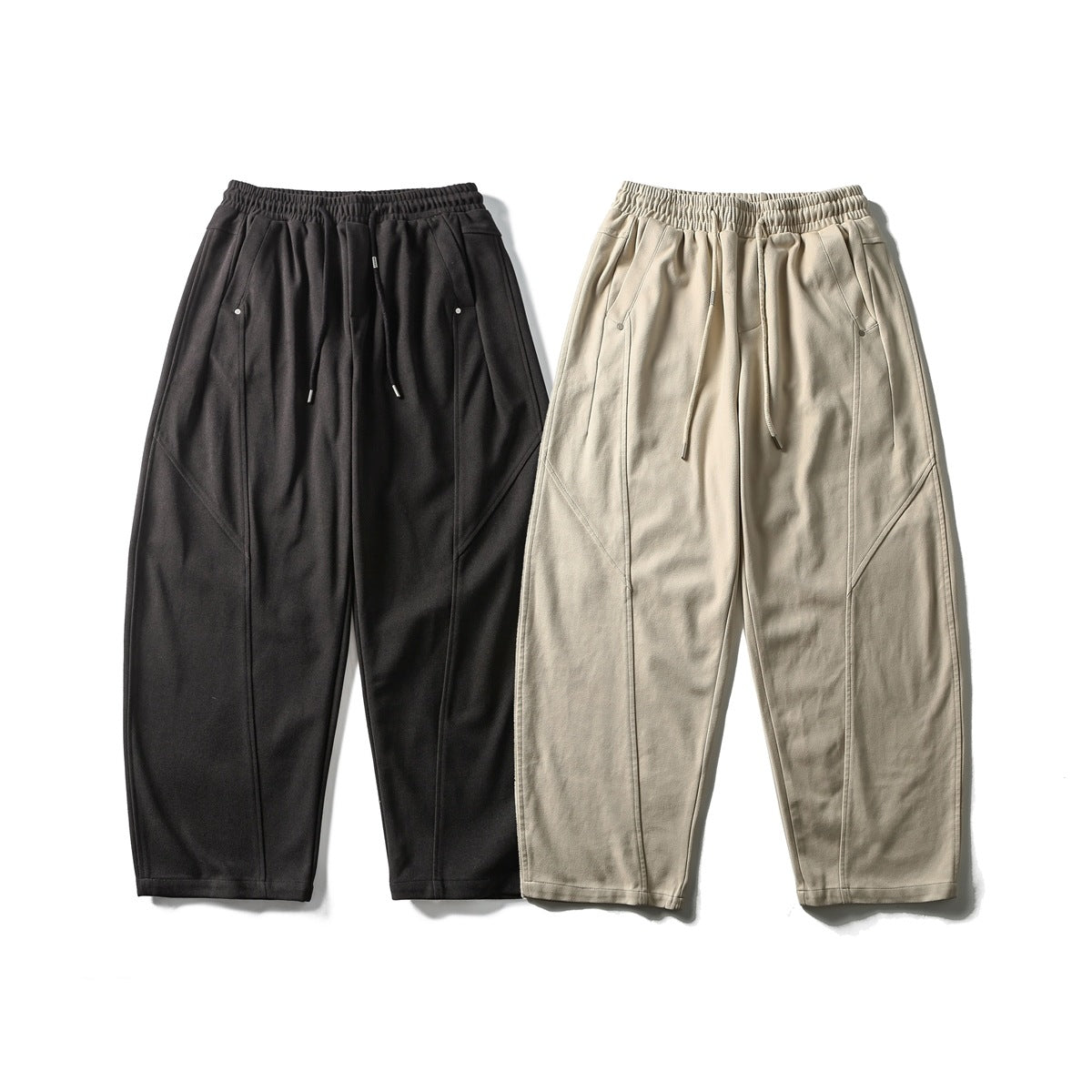 Front view of relaxed black and beige pants with elastic drawstring waists, angled pockets and curved seam panels.