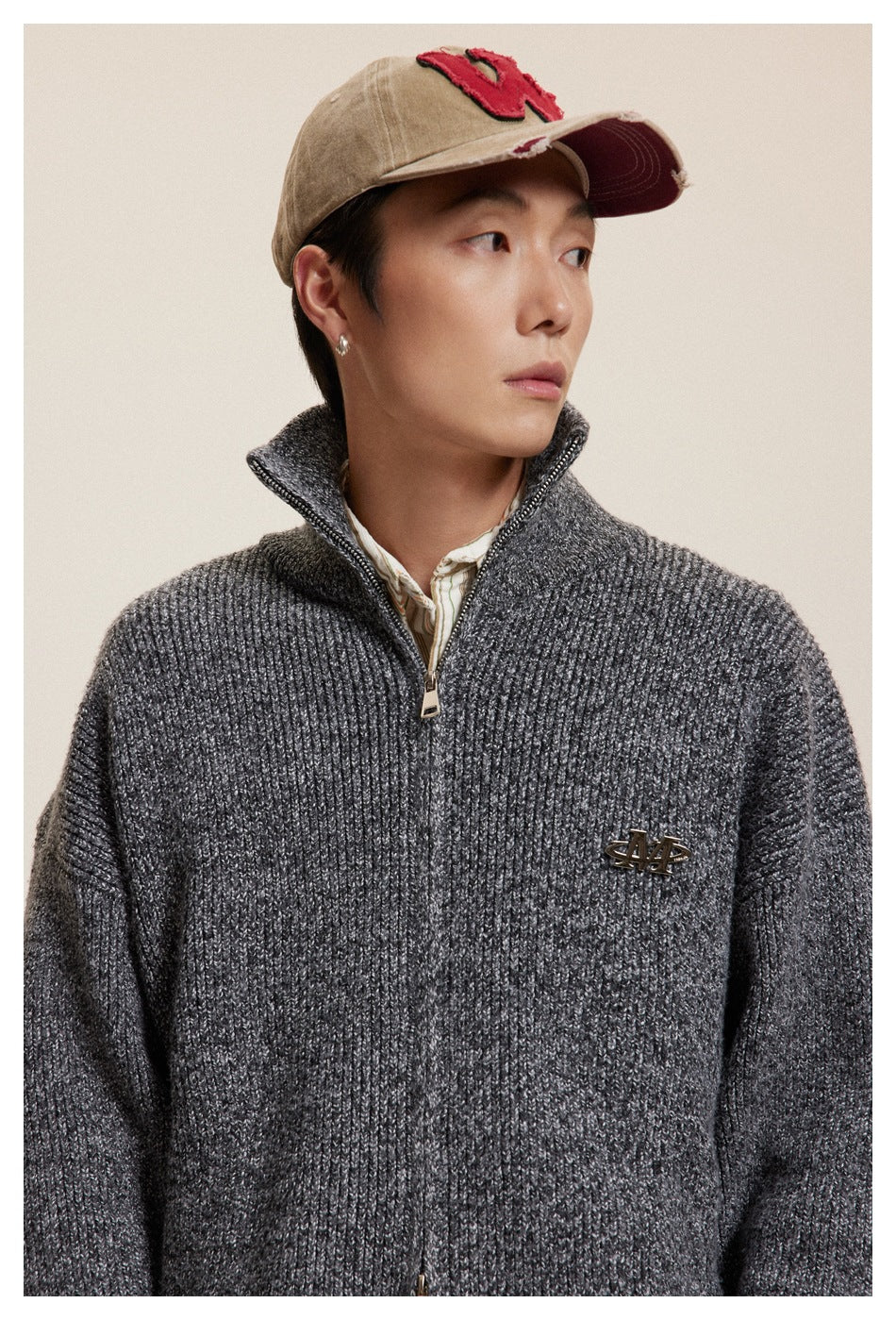 Close-up of a model wearing a charcoal textured zip-up cardigan with a raised collar and a small metal chest emblem.