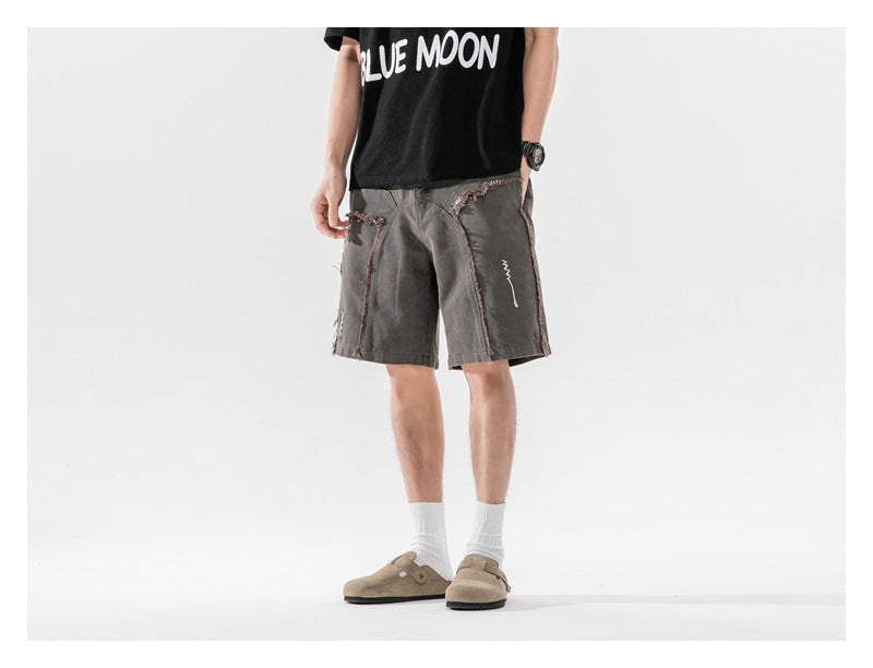 Person wearing dark gray frayed-seam shorts with a black graphic tee, white socks and tan clogs, angled view