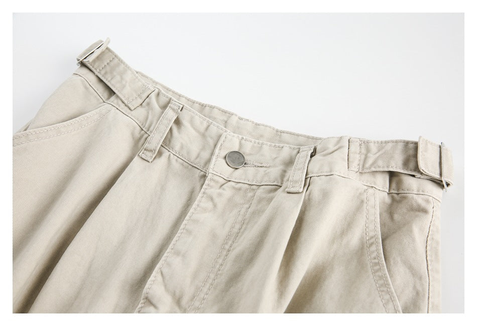 Front view of beige trousers laid flat, showing the waistband, button, belt loops, and adjustable side tabs.