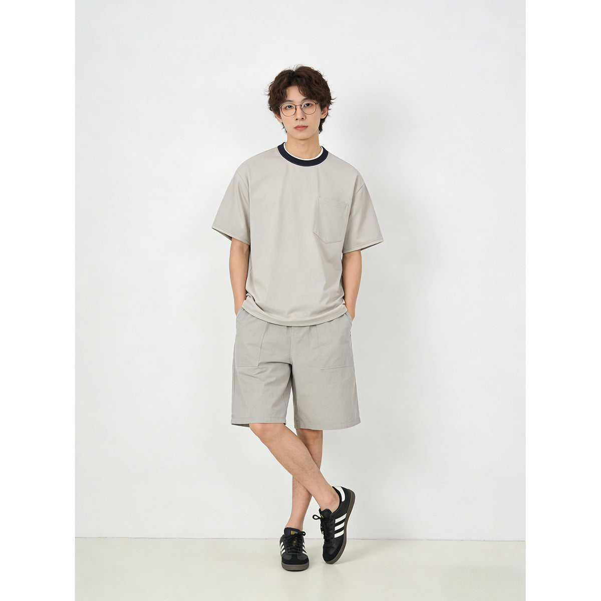 Front view of a model wearing a light gray pocket T-shirt with a dark contrast collar and matching shorts.