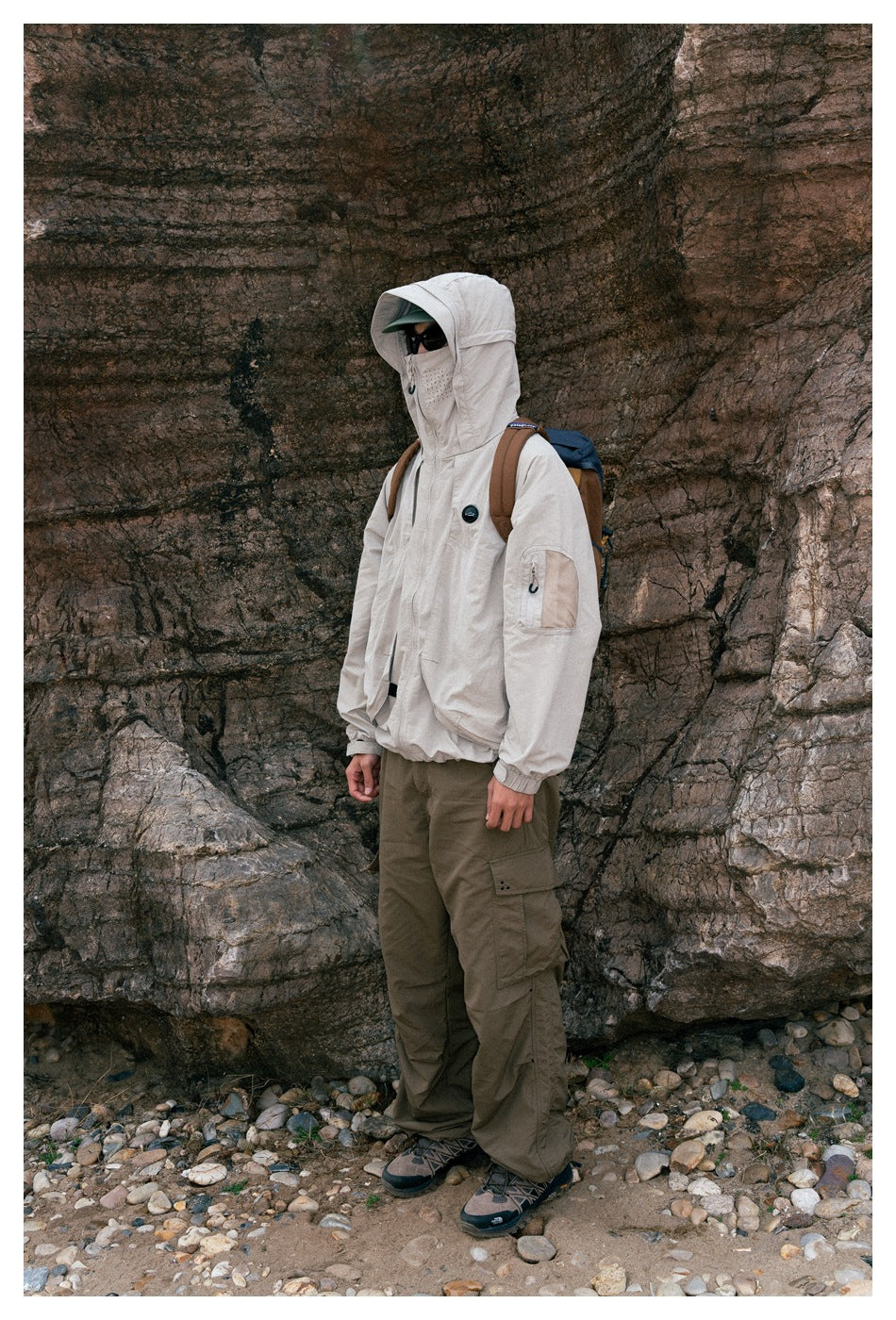 Side view of a person wearing a light beige hooded jacket with the hood up and olive cargo pants.