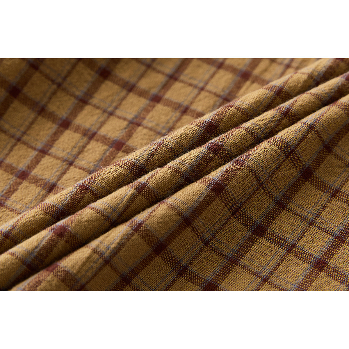 Close-up showing the brown and muted red plaid pattern and folds of the shirt fabric.