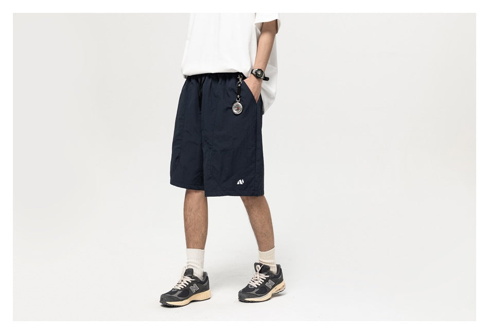 Man wearing navy knee-length shorts with a white tee and sneakers, side view with hand in pocket
