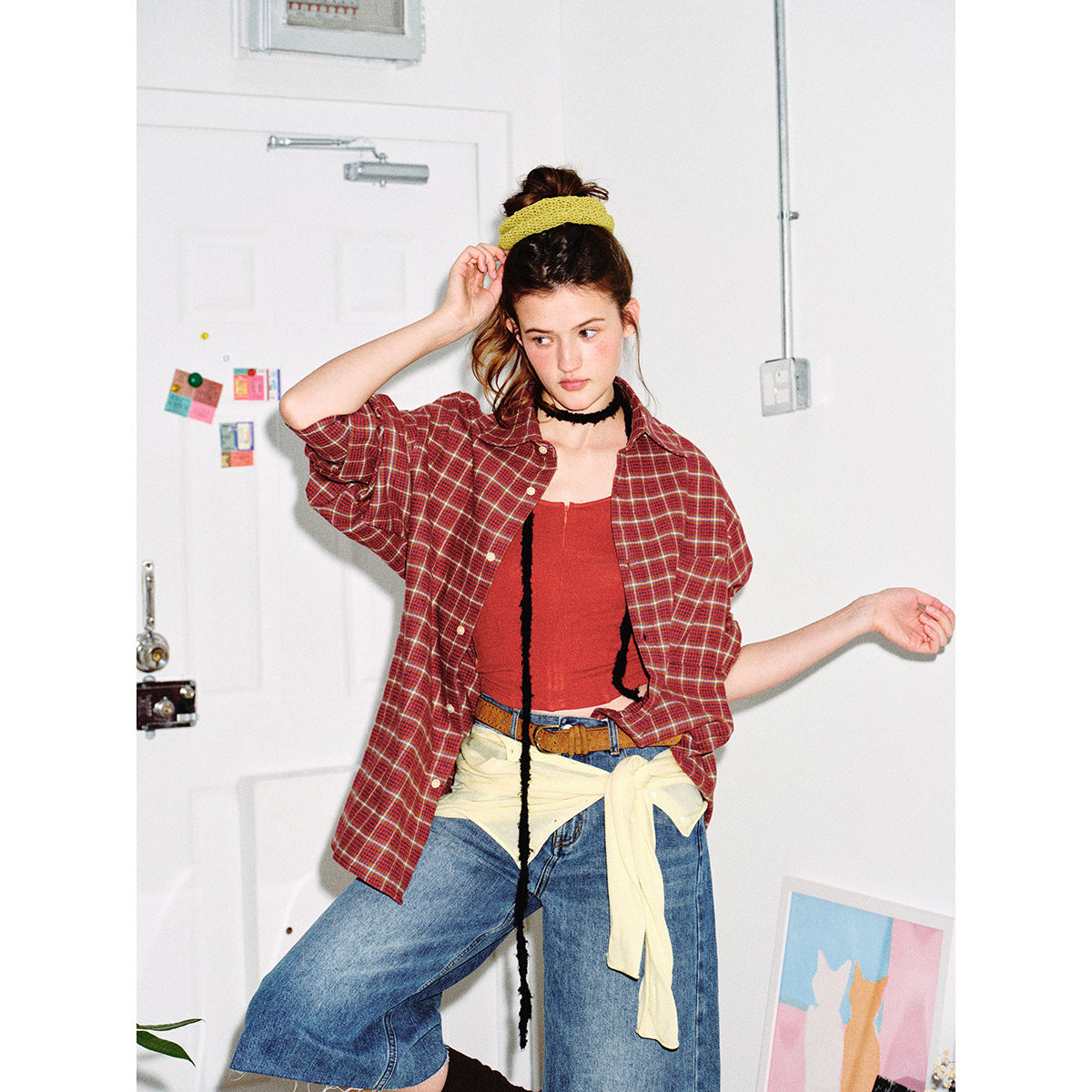 Model wearing a loose red plaid button-up shirt over a red top, with rolled sleeves and a chest pocket.