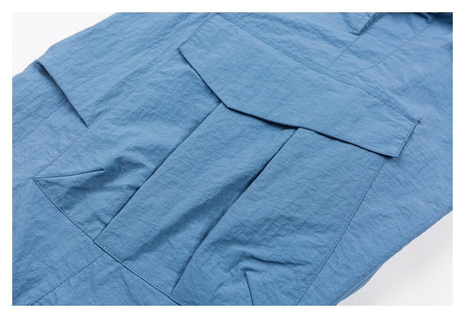 Close-up of blue garment fabric with a large layered rectangular pocket and flap.