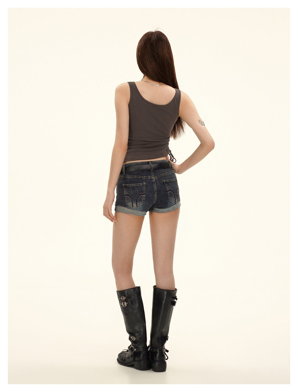 Rear view of a model wearing a charcoal sleeveless top and dark cuffed denim shorts with black knee-high boots.