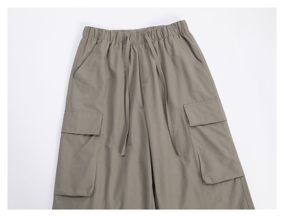Close-up of taupe cargo pants showing the elastic drawstring waist, slanted hand pockets, and large flap side pockets.