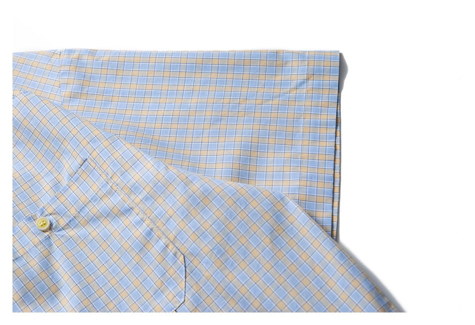 Close-up of a light blue and tan plaid shirt laid flat, showing a button and chest pocket.