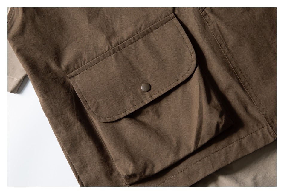 Close-up of a dark brown garment's large snap-flap pocket and surrounding seams.