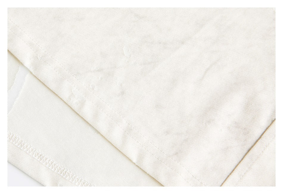 Close-up of an ivory garment hem with visible stitching and mottled distressed fabric.