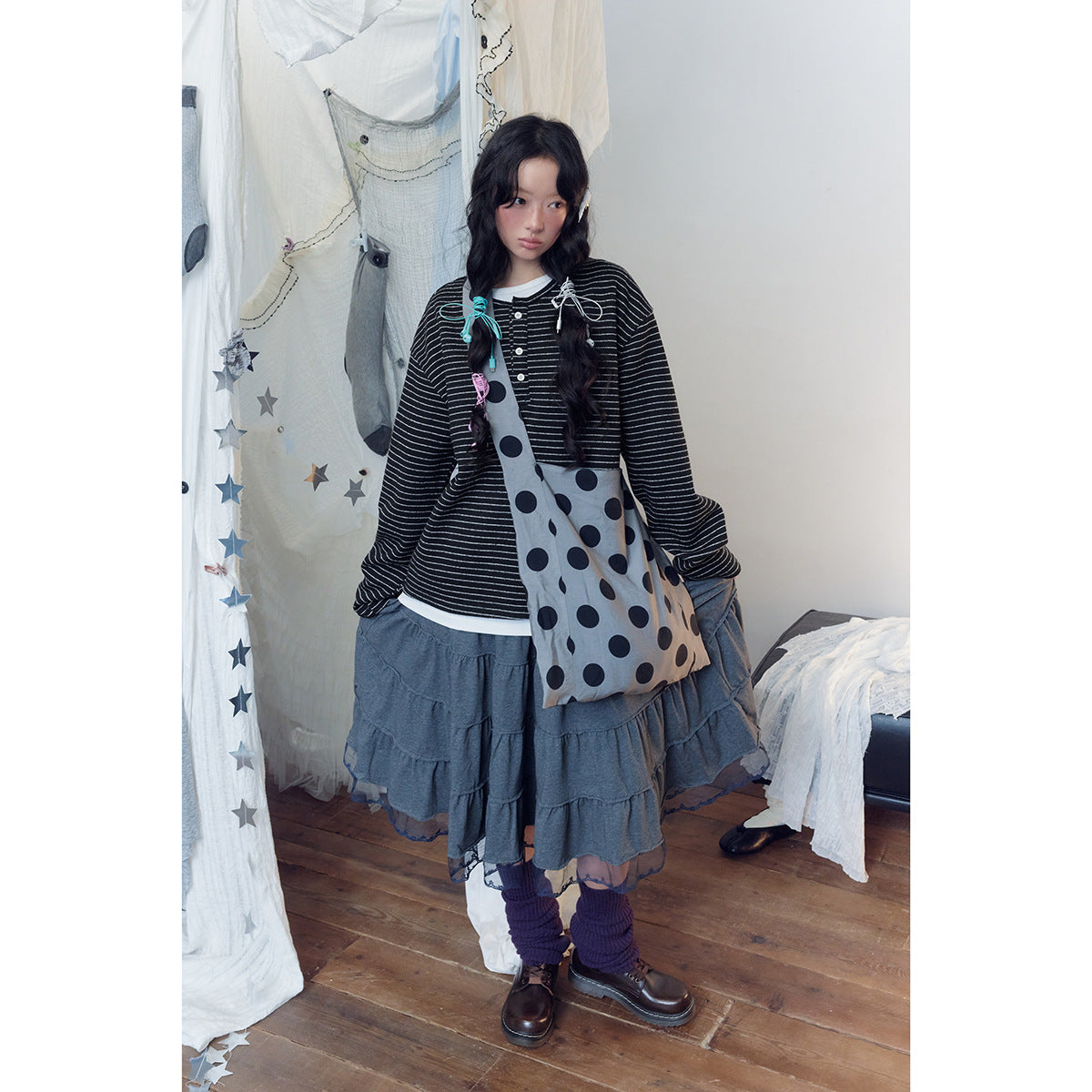 Model wearing a black-and-white striped long-sleeve henley with a gray polka-dot shoulder bag and tiered skirt.