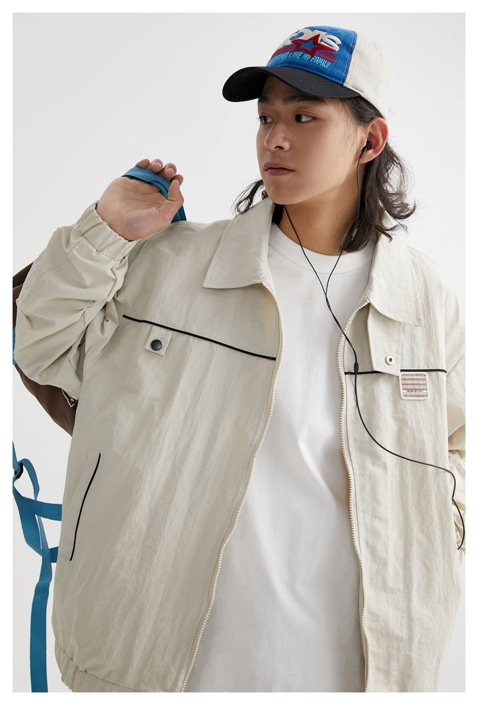 Close view of a model wearing an ivory jacket with black piping, a zip front and a chest patch.