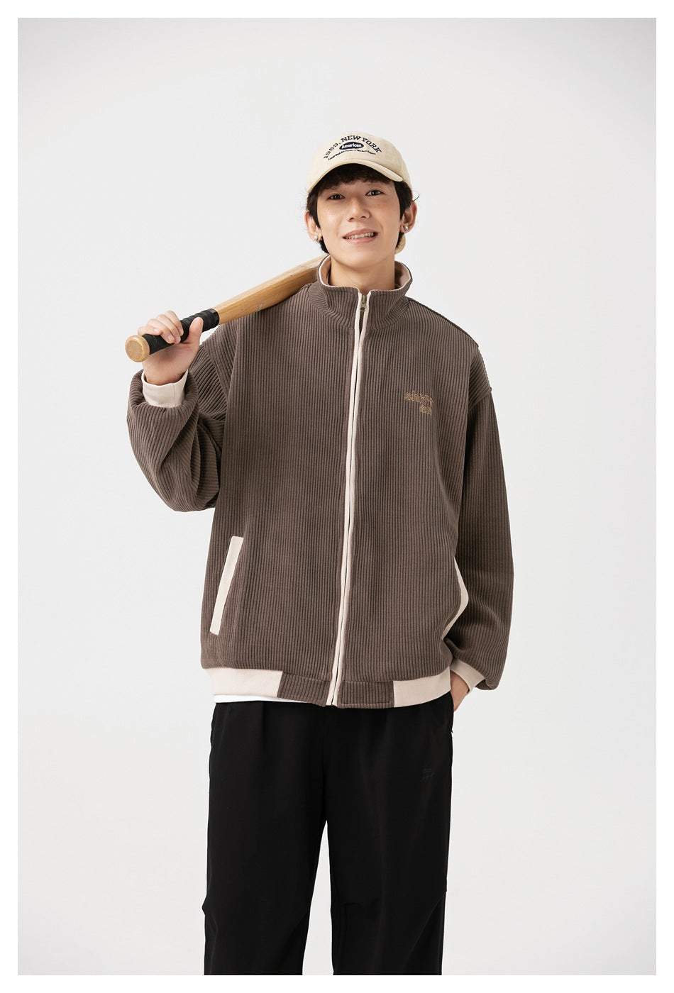Model wearing a taupe ribbed zip-up jacket with cream trim, standing against a light background.