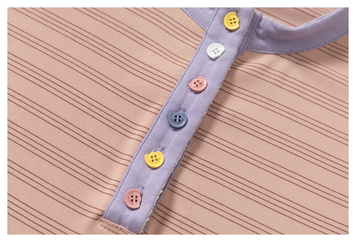 Close-up of a lavender placket with yellow, white, pink, and blue buttons on peach-pink striped fabric.