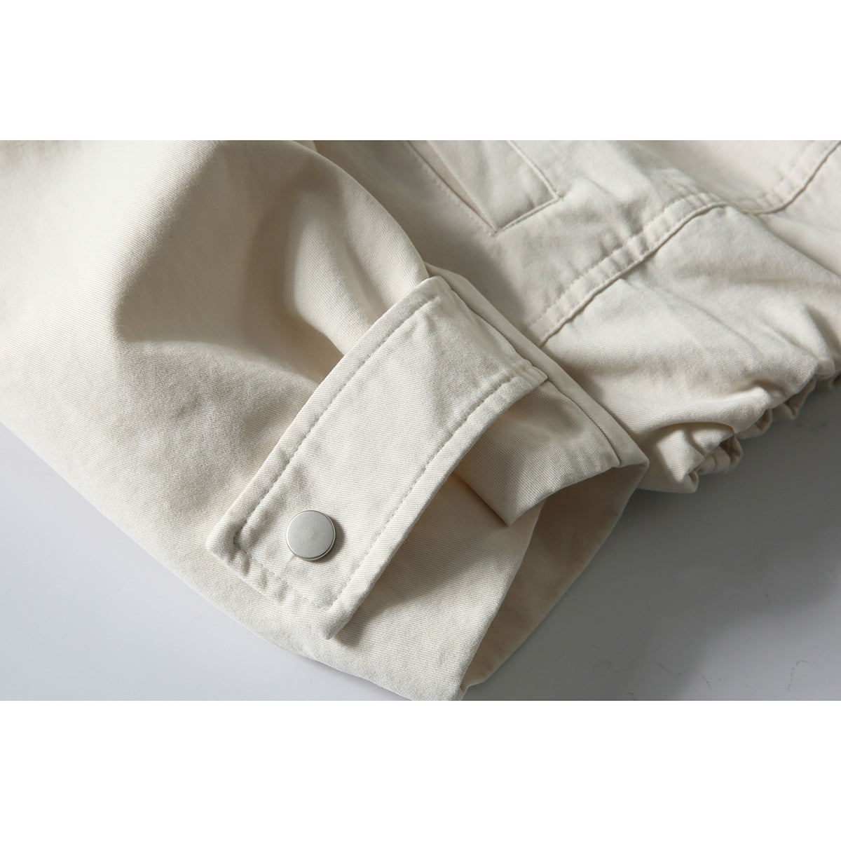 Close-up of an off-white jacket sleeve cuff with a large round snap and gathered fabric nearby.