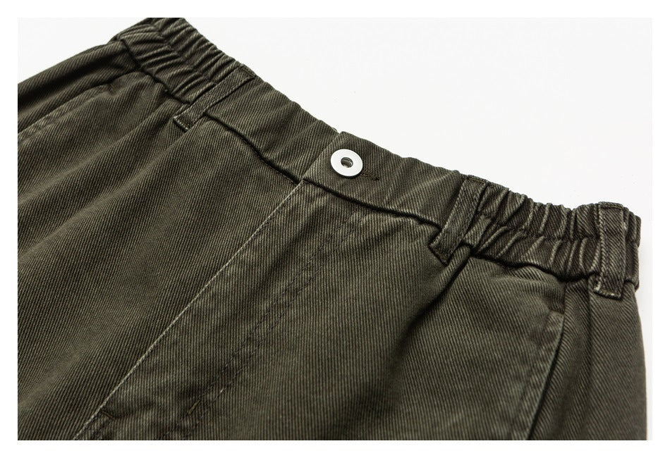 Close-up of olive-brown trousers showing the elastic waistband, belt loops, and button closure.
