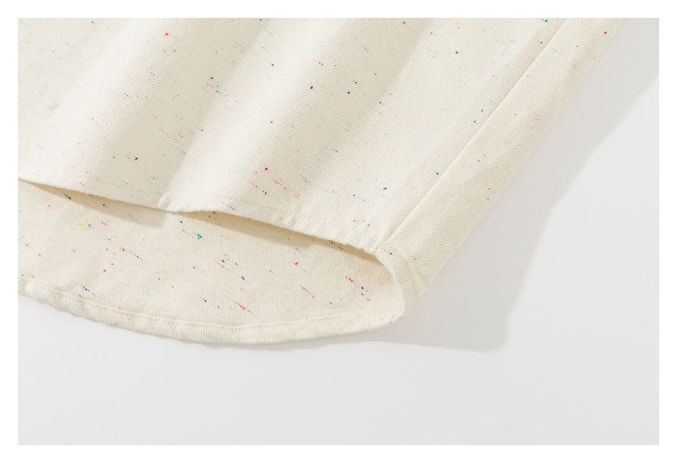 Close-up of the curved hem of an off-white garment with scattered multicolor flecks.