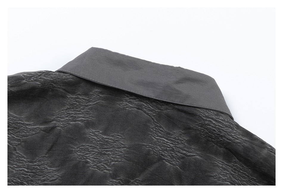 Close-up of a charcoal garment showing a smooth flap above a crinkled textured panel.