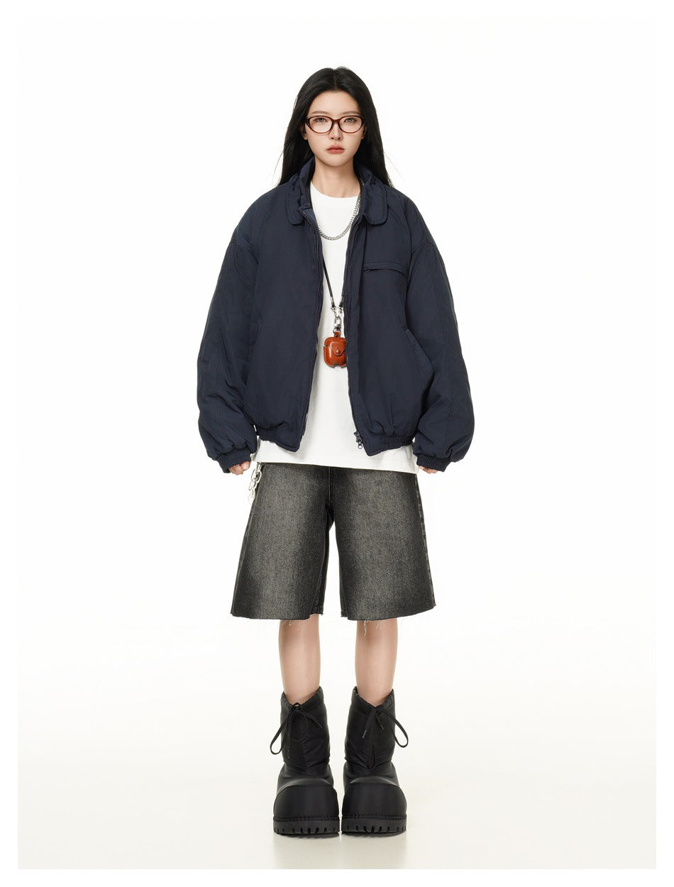 Full-length front view of a model wearing an oversized navy jacket with a white shirt, dark shorts and black boots.