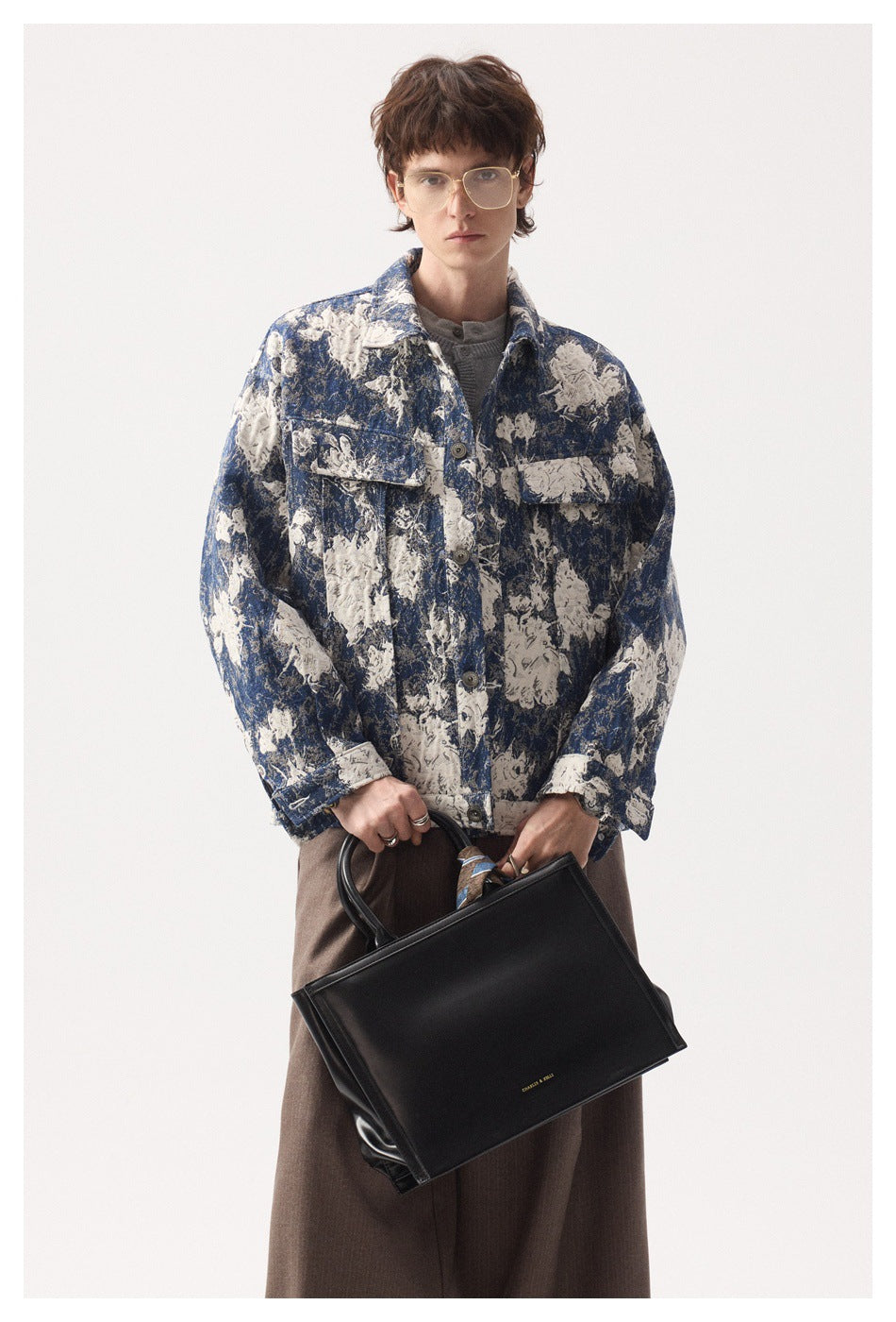 Front view of a model wearing a blue and cream floral button jacket, holding a large black handbag.