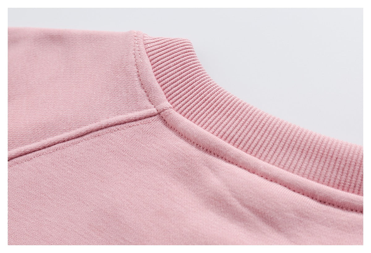 Close-up of a pink garment's ribbed crew neckline and stitched shoulder seam.