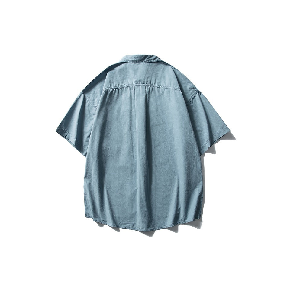 Back view of a light blue short-sleeve collared shirt with a center pleat and curved hem, displayed against white.