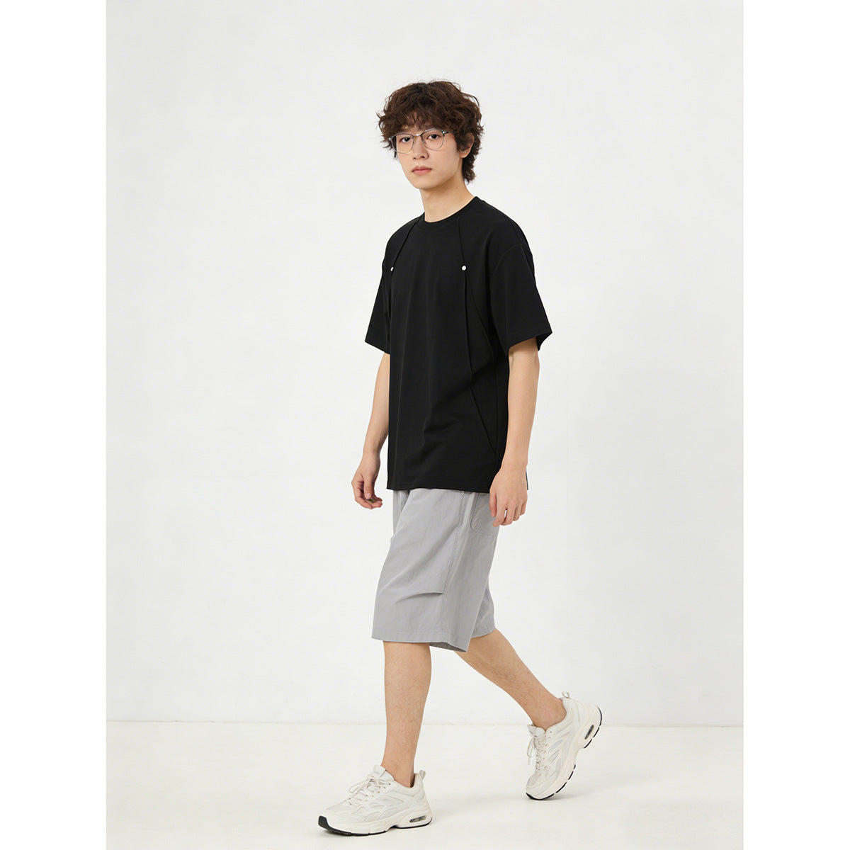 Model wearing a black short-sleeve tee with curved front panels and small snaps, paired with gray shorts.