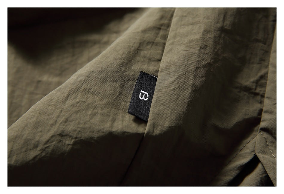 Close-up of an olive-brown shirt seam with a small black woven label bearing a white symbol.