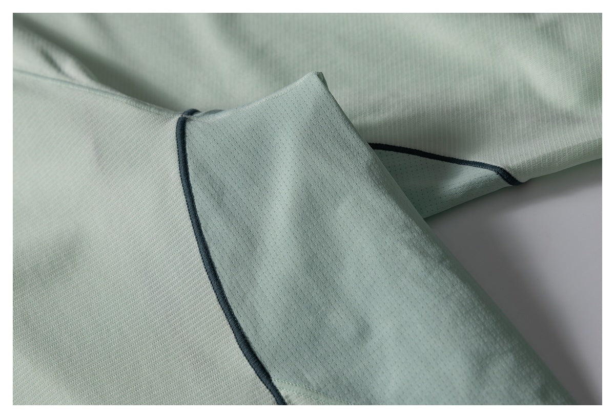 Close-up of a pale mint-green garment showing a sleeve and dark contrast piping along the seams.