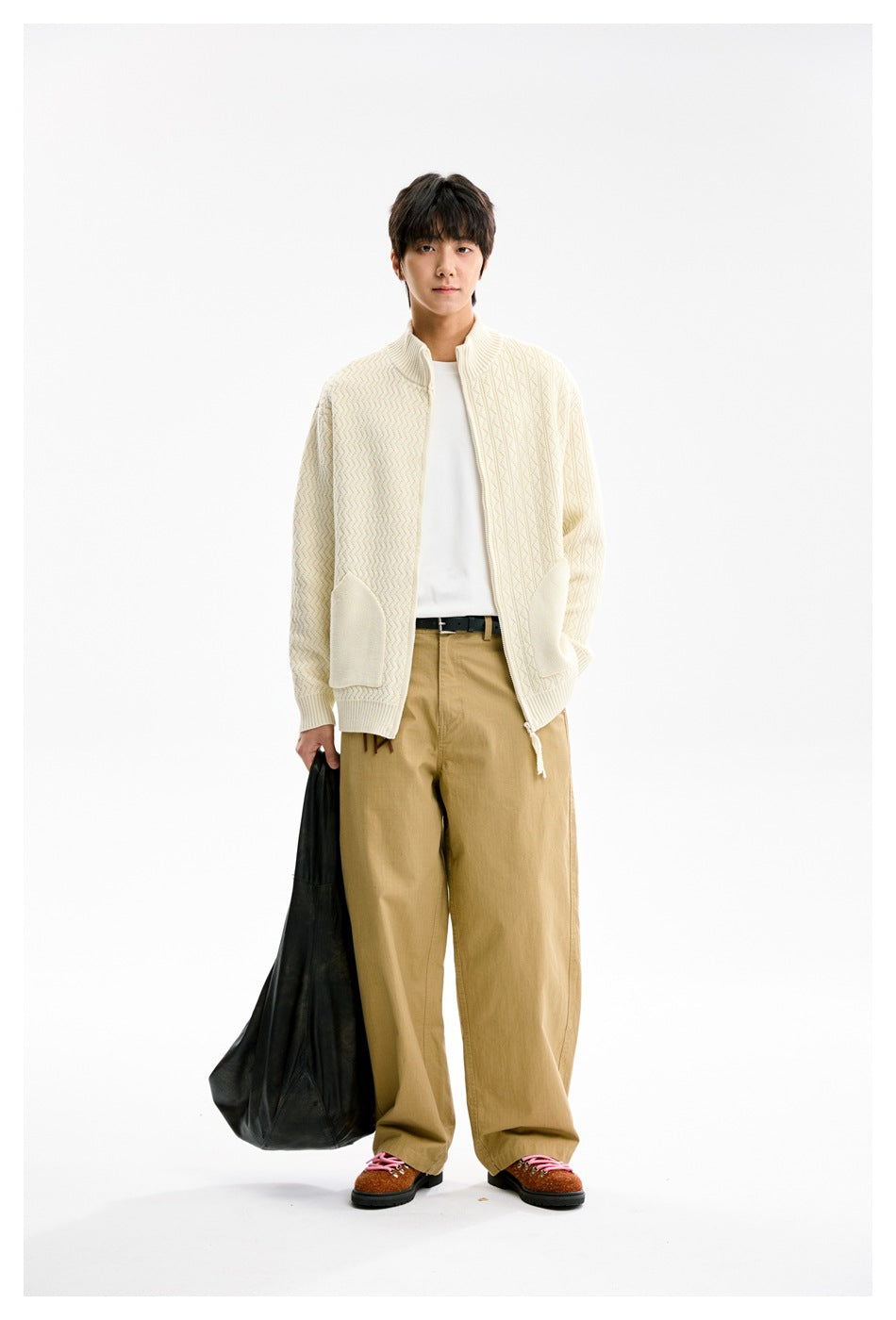 Model wearing apricot knit zip cardigan open over a white tee with khaki wide pants, holding a black bag