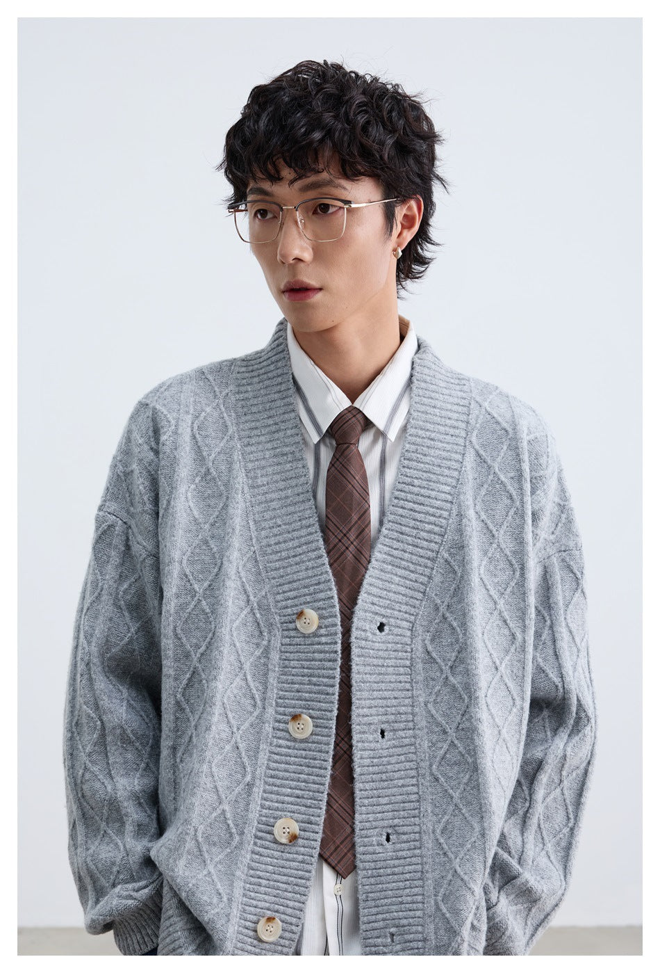Close view of a model wearing a light gray diamond-knit cardigan over a striped shirt and tie.