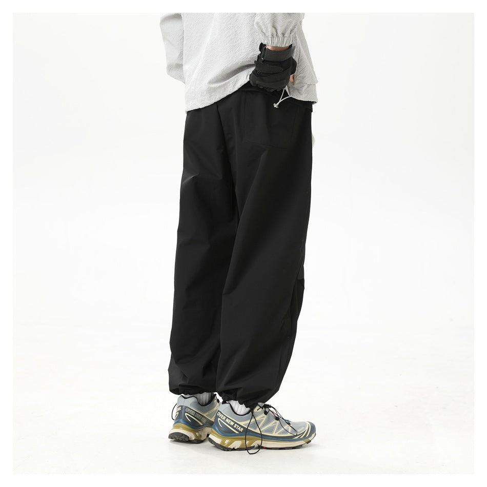 Back view of a model wearing black relaxed pants with gathered ankle cuffs, a gray top and sneakers