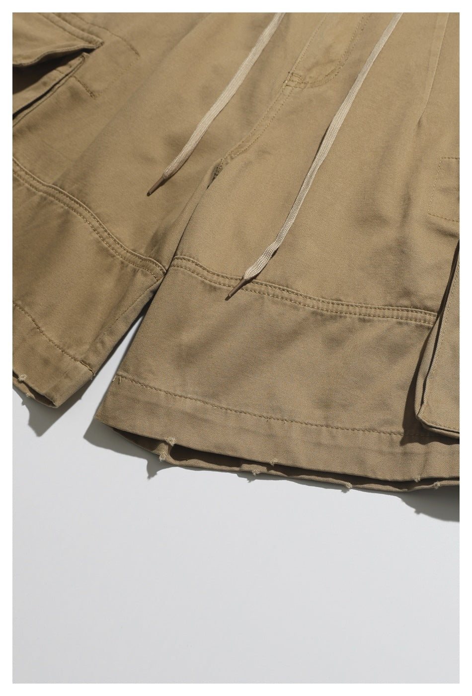 Close-up of khaki trouser legs with pale drawcords, stitched panels, and cargo pockets.