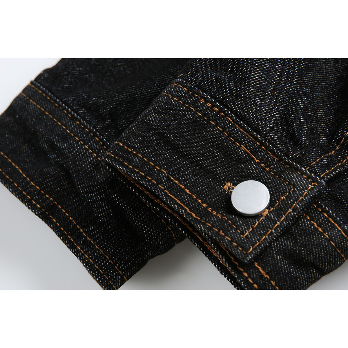 Close-up of a black denim sleeve cuff with a silver snap and orange topstitching.