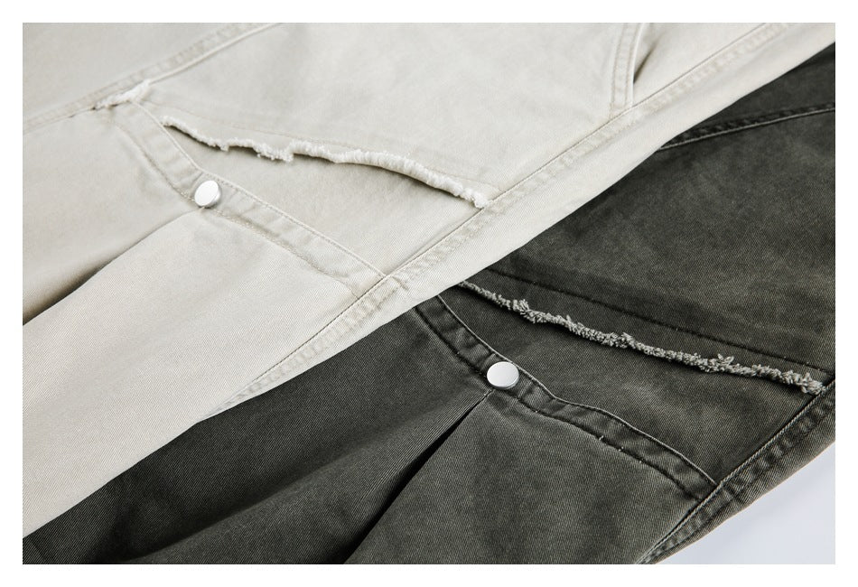 Close-up of ivory and charcoal pants with frayed knee seams, silver buttons and pleated panels.
