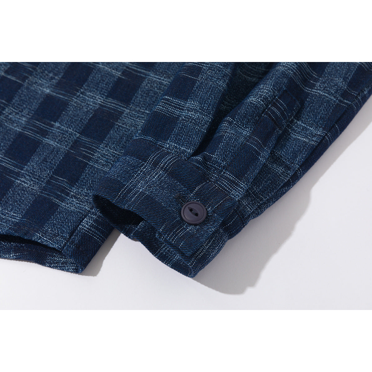 Close-up of a navy plaid shirt sleeve cuff with a dark button.