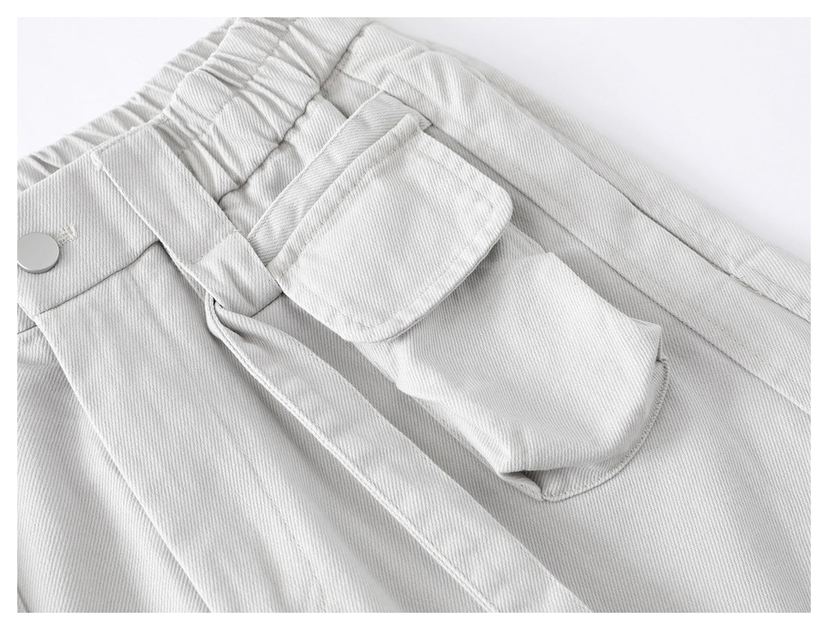 Close-up of a light gray trouser utility pocket with a flap, beside the elastic waistband and belt loop.