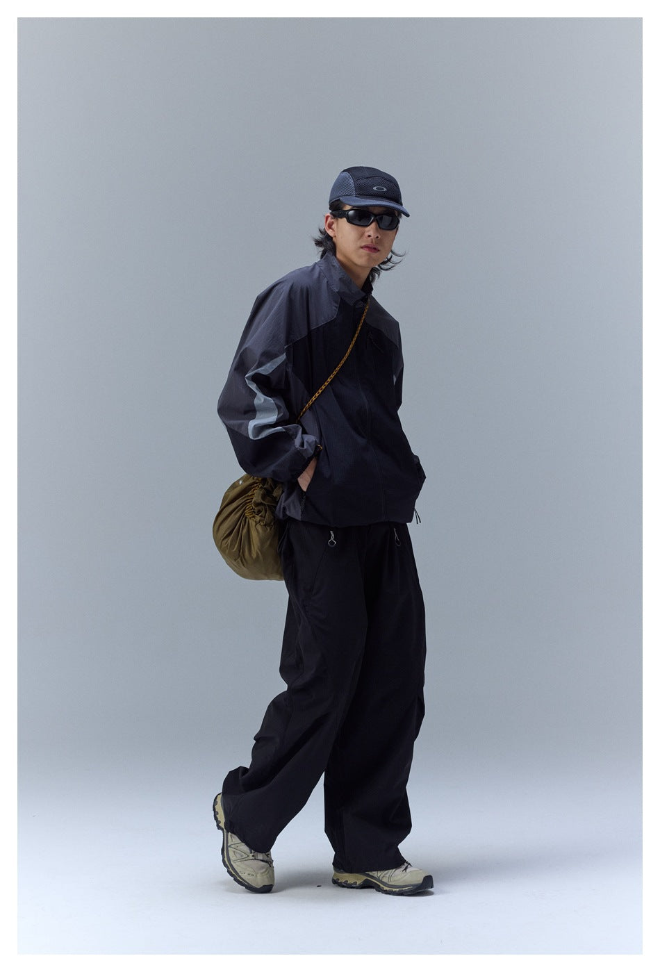 Person wearing the black and charcoal color-block zip jacket with black pants, side view with hand in pocket