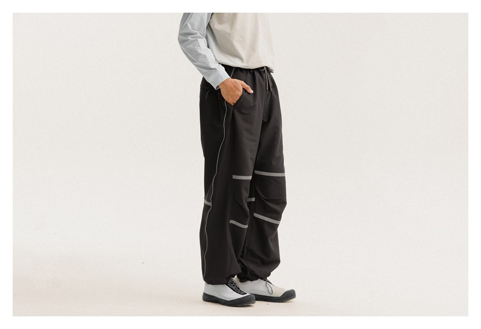 Side view of a model wearing loose black drawstring pants with gray bands across the legs.