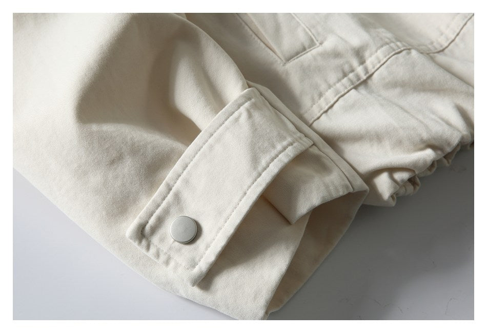Cream jacket sleeve cuff with a round metal snap and gathered fabric nearby.