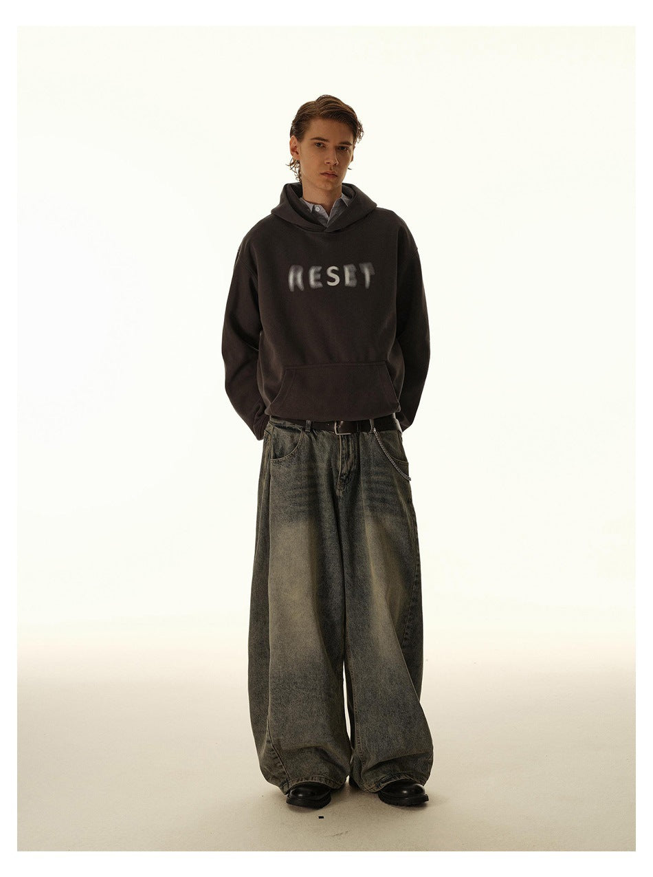 Model wearing a dark brown hoodie with blurred chest lettering and extremely wide gray-black jeans.