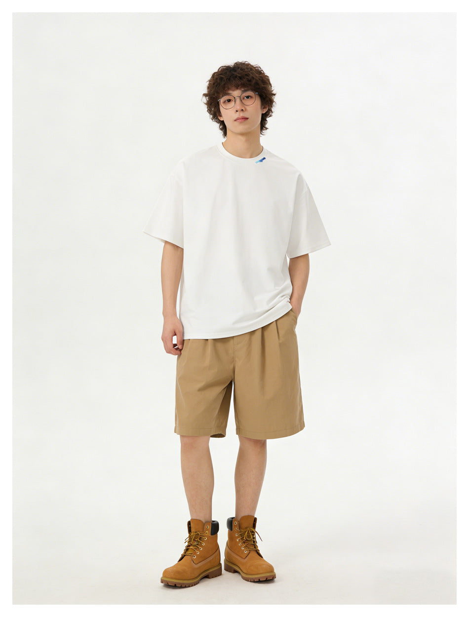 Model wearing an oversized white T-shirt with a small blue collar detail, tan shorts, and brown lace-up boots.