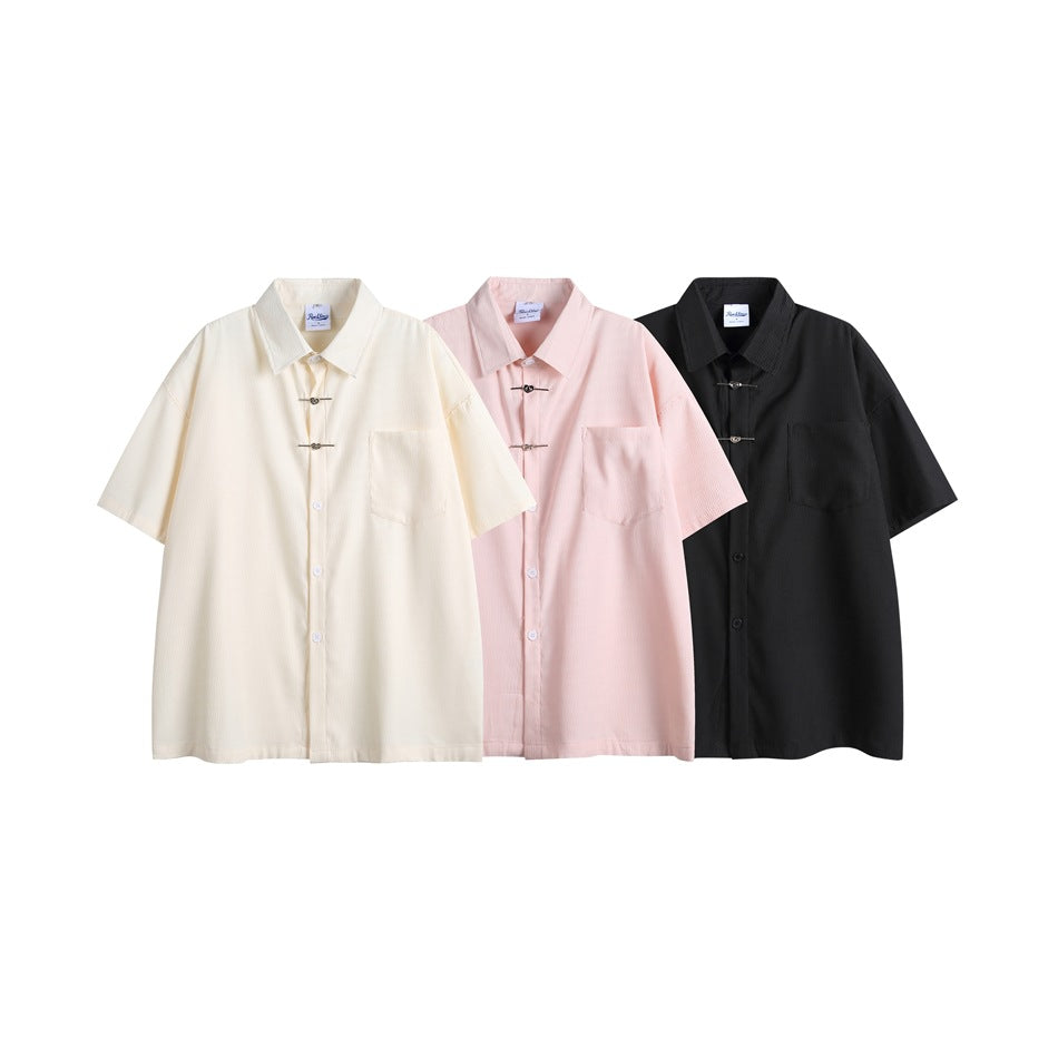 Three short-sleeve collared shirts with metal toggles shown in cream, pale pink, and black.