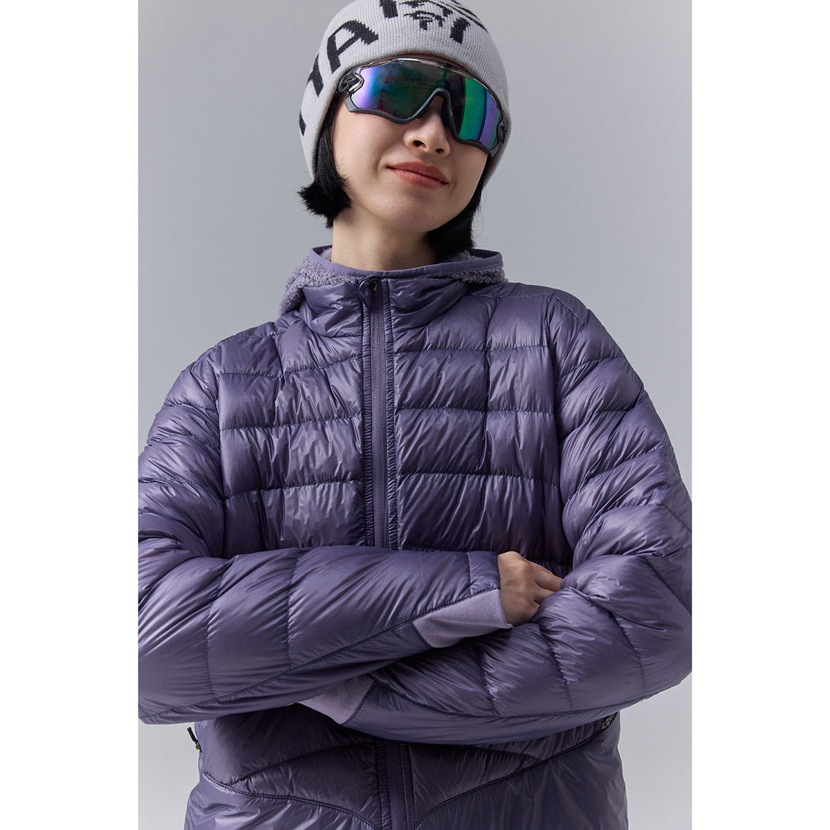 Close view of a model in a shiny lavender quilted jacket with a hood and front zipper.