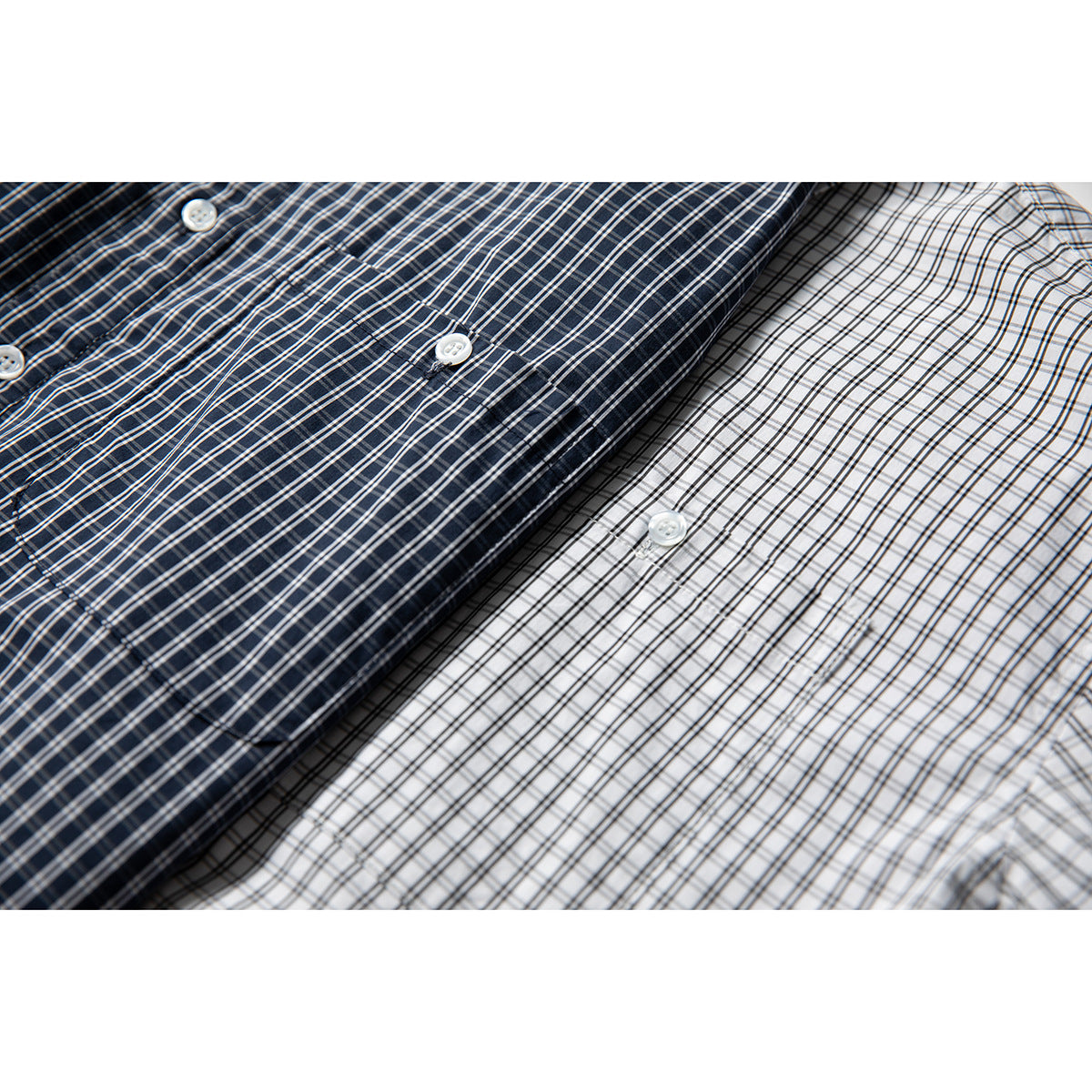 Close-up of overlapping navy and white plaid button-up shirts with white buttons.