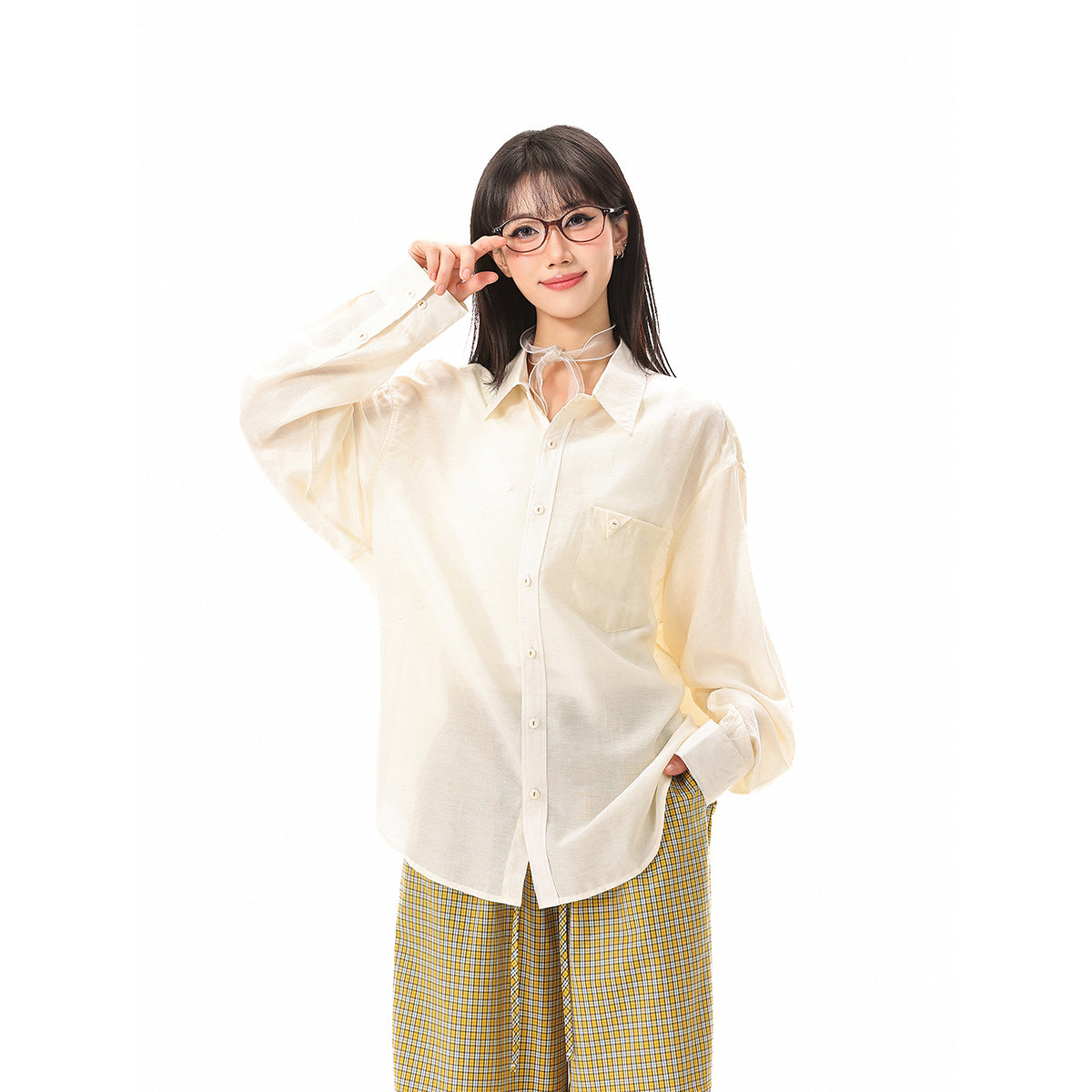 Model wearing an oversized ivory button-up shirt with a chest pocket and yellow plaid trousers.