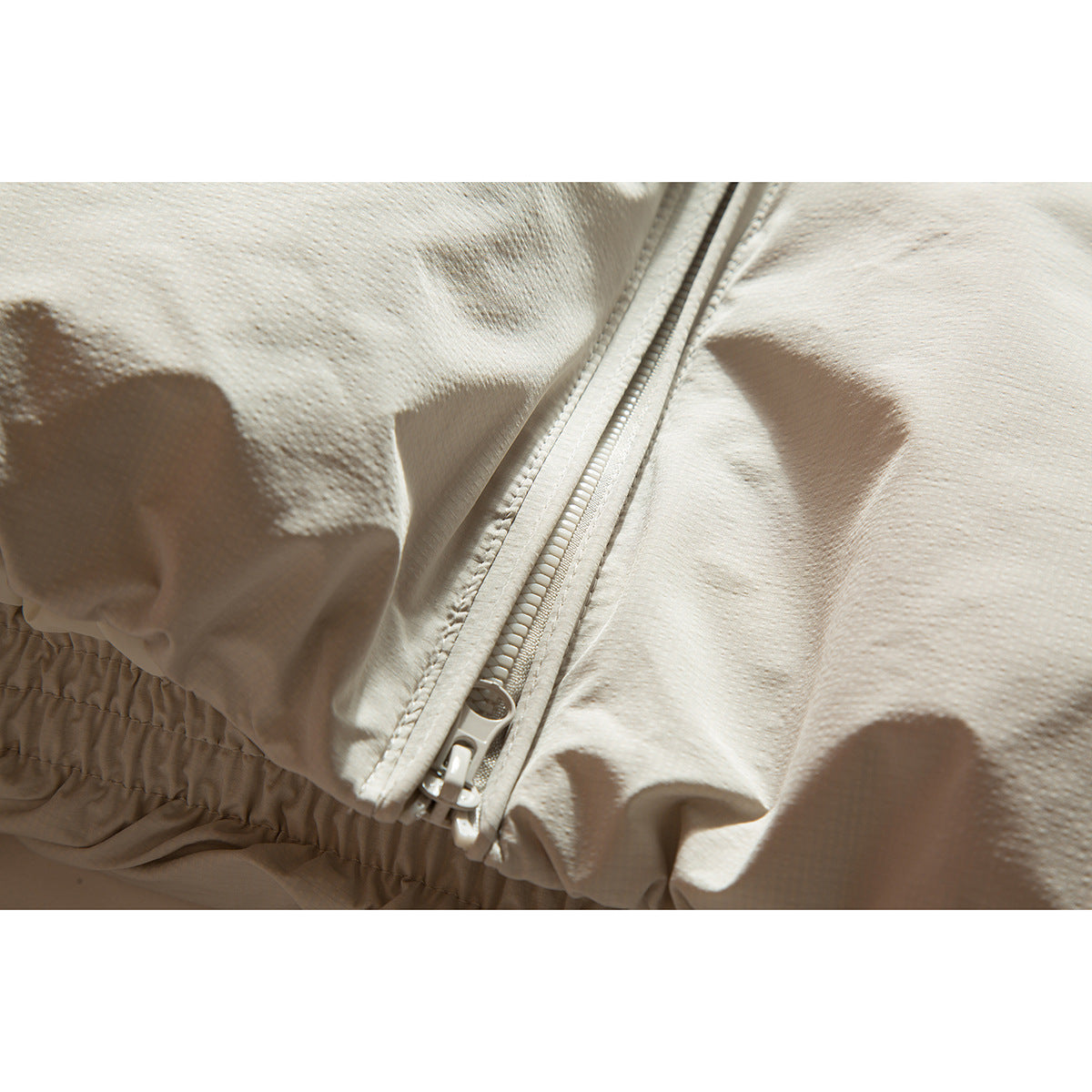 Close-up of the off-white jacket's zipper and gathered elastic hem.