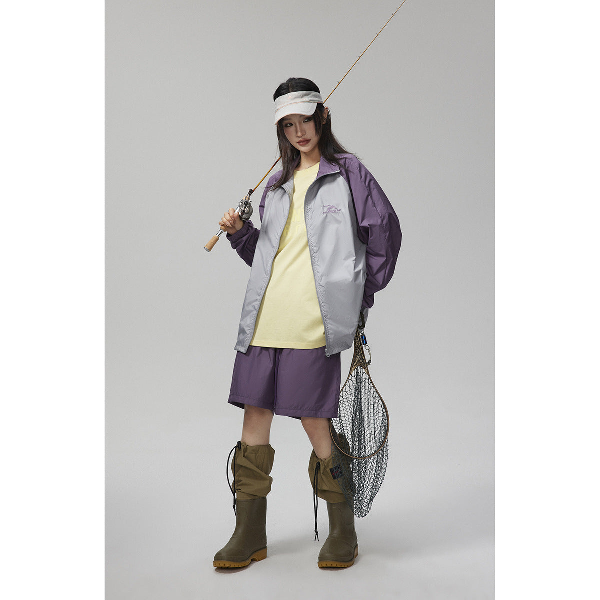 Model wearing a gray jacket with purple sleeves, pale yellow top, purple shorts, and olive rain boots.
